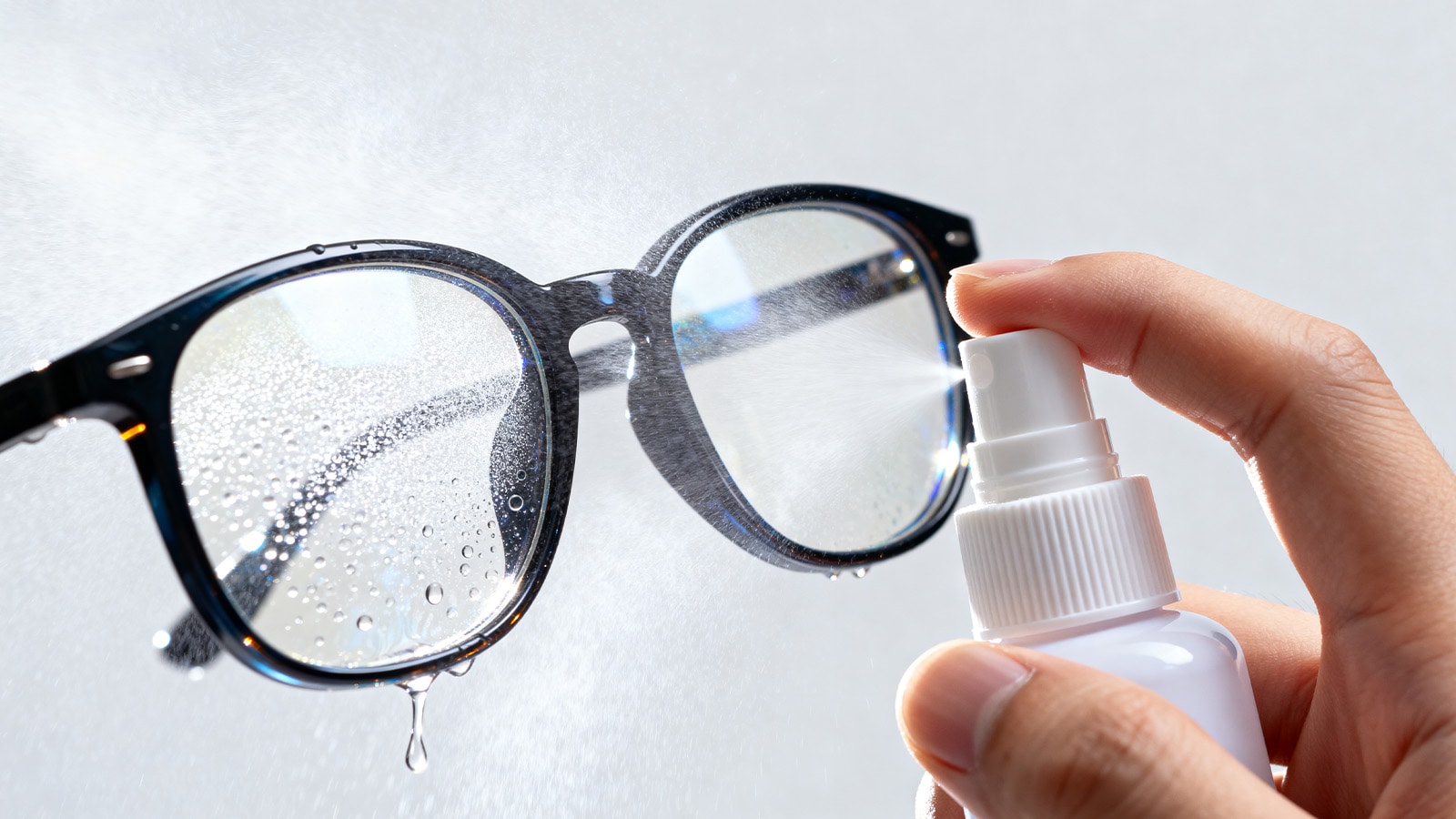A hand uses an anti-fog spray on eyeglass lenses as a quick fix to prevent them from fogging up.