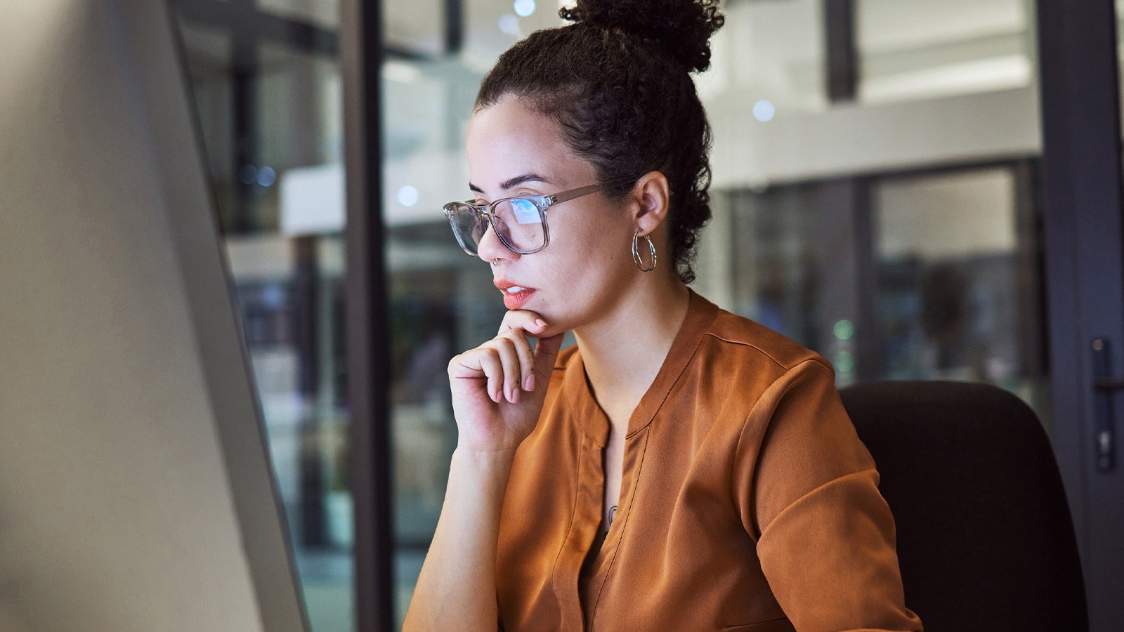 A woman wearing blue-light blocking glasses over her contacts to protect her eyes from digital eye strain while working on a computer.