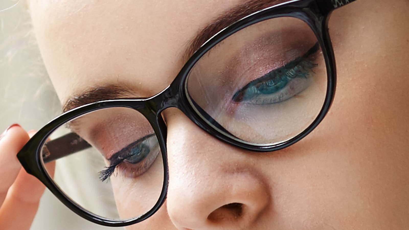 Close-up of woman's eyes with black glasses and subtle blue eyeshadow, emphasizing makeup visibility through frames.
