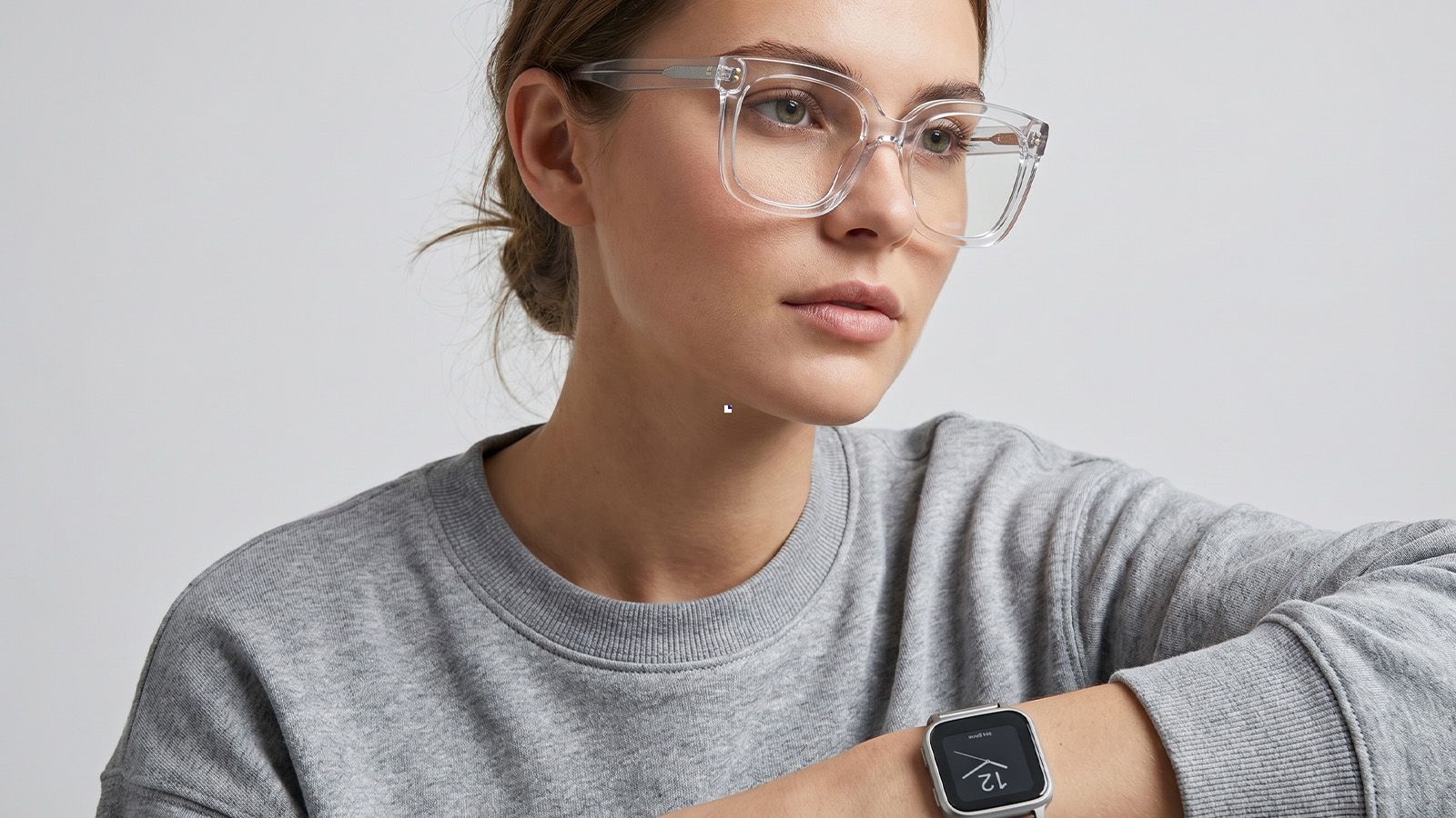 High-definition portrait of a model wearing crystal clear acetate frames with bold, ice-like transparency. The high-clarity glasses create a subtle tonal match with the textured heather grey minimalist round-neck sweatshirt, highlighting premium material finish. Professional San Francisco glasses style.