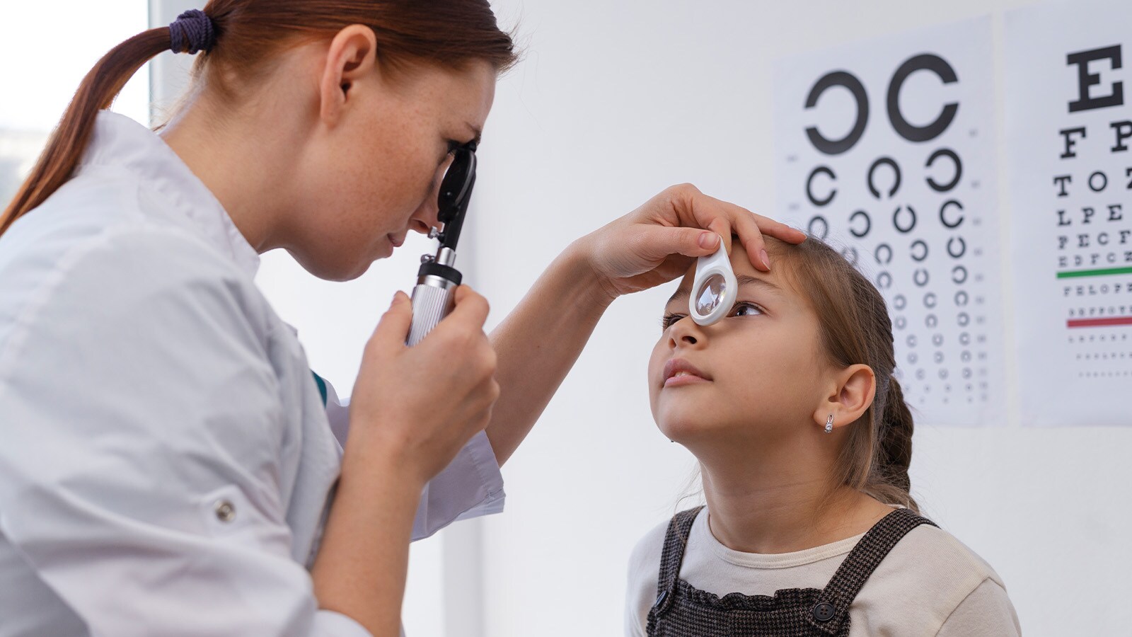 Eye doctor performing a comprehensive eye exam on a girl to check if a child needs glasses.