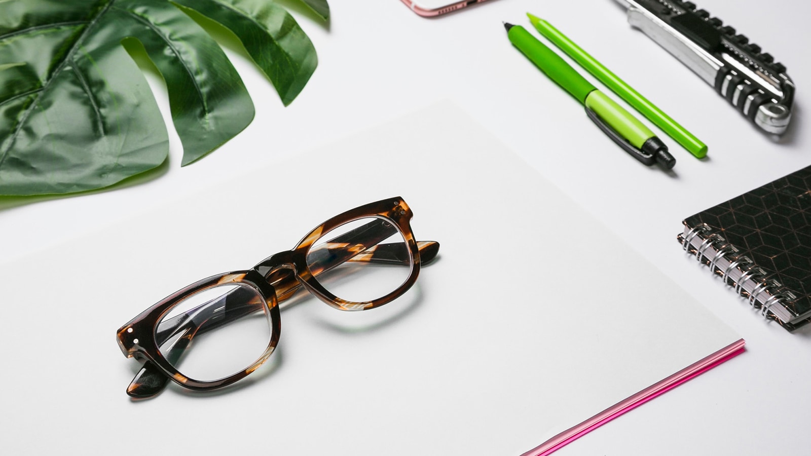 A pair of tortoise-shell glasses sits on a blank notepad.