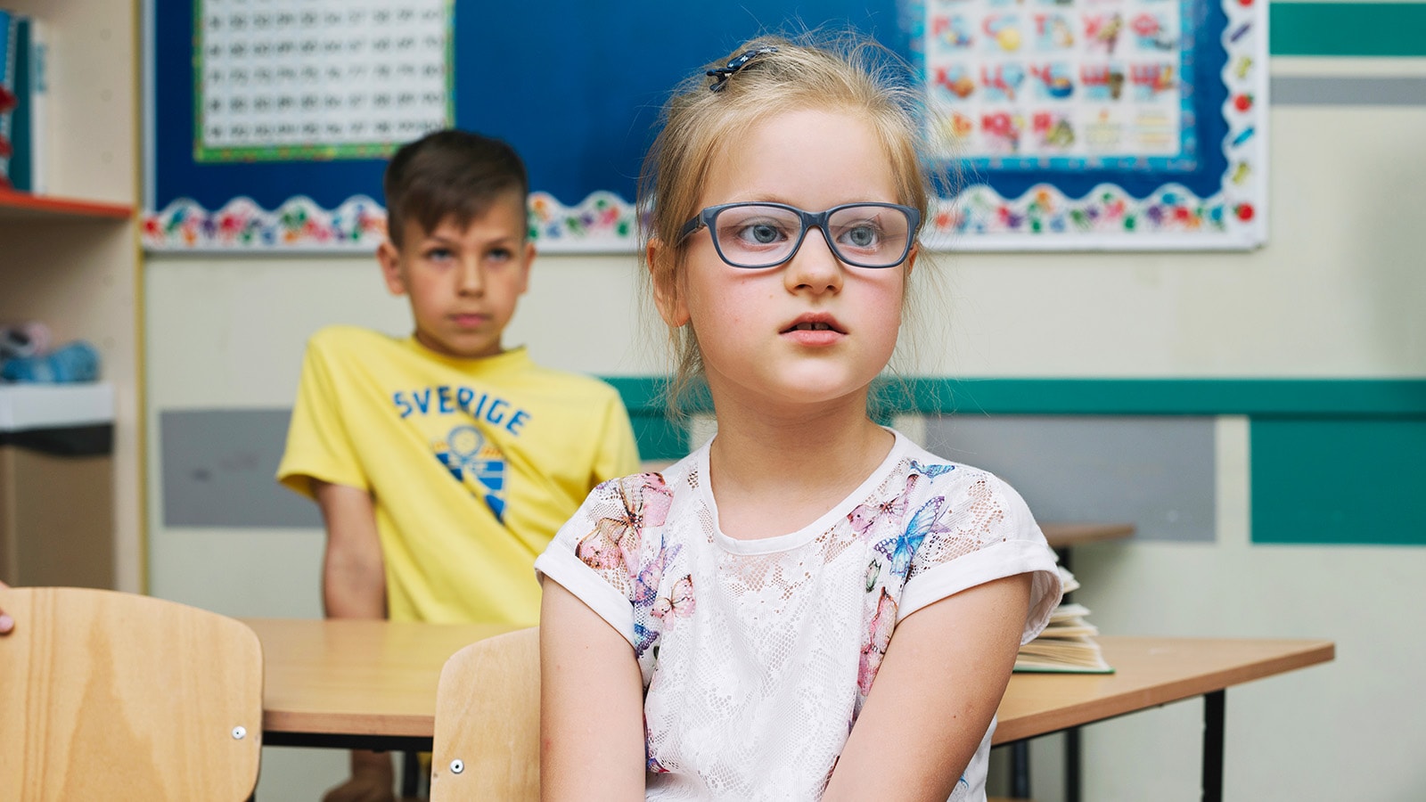 Girl in class squinting, a key sign a child needs glasses to see the board.
