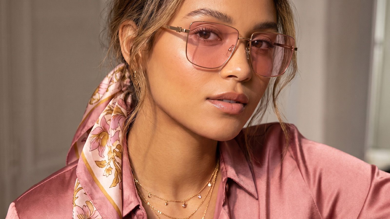 Close-up of a model wearing pink tinted metal frames paired with gold jewelry for a stylish, coordinated fashion look.