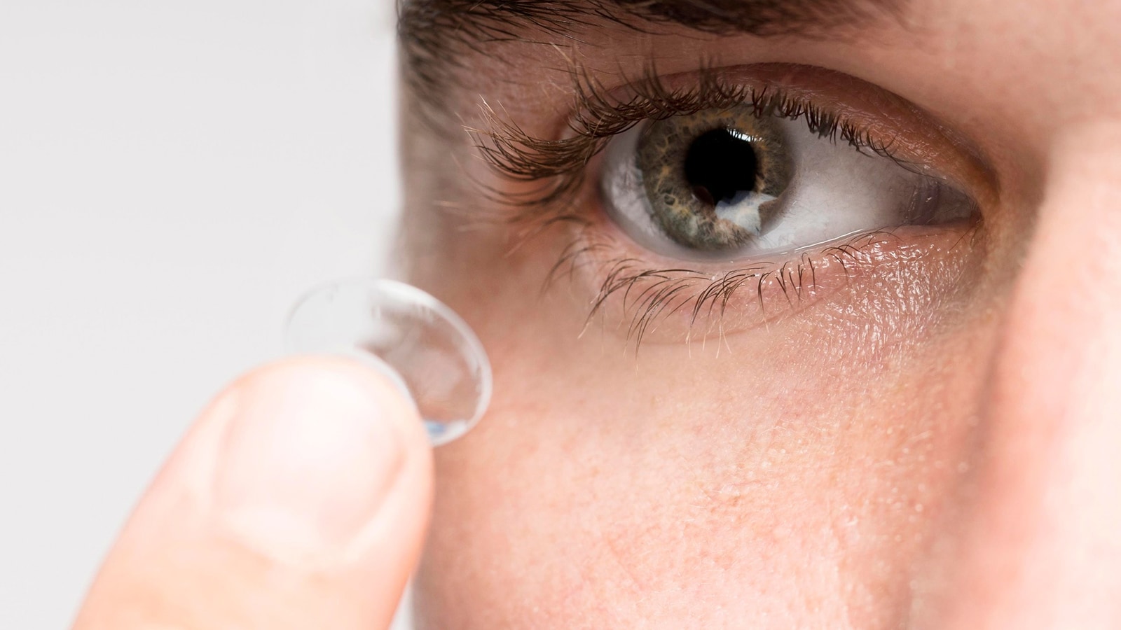 A close-up of a person's finger holding a contact lens, about to place it in their eye.