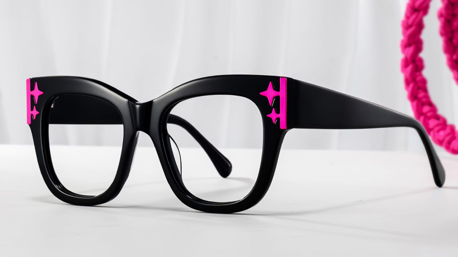 A pair of black prescription cats-eye glasses with pink star-shaped details on the frames.