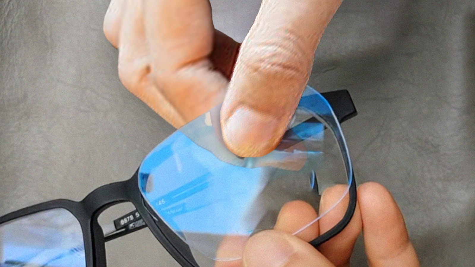 A person's hands carefully reinserting a clear lens into a black glasses frame, demonstrating the alignment step.