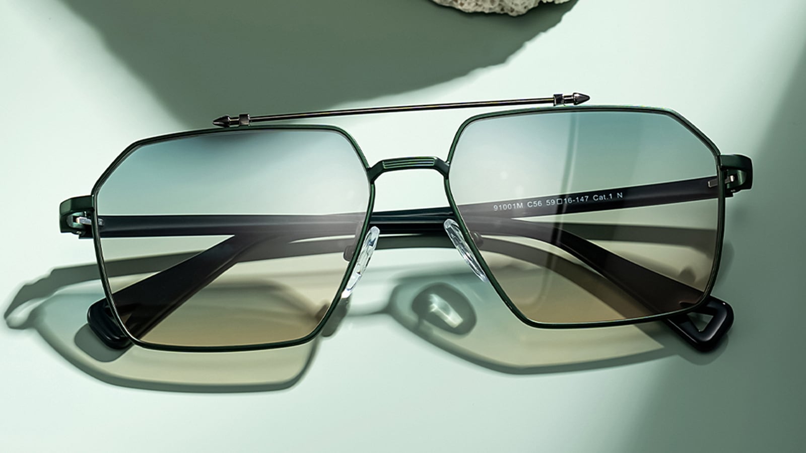 A pair of stylish, dark-framed blue light blocking glasses with a slight gradient tint on a light green surface.