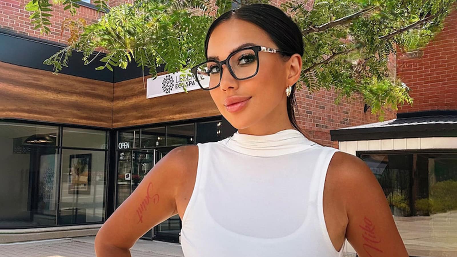 A stylish woman wearing a white top and a pair of fashionable eyeglasses outdoors.