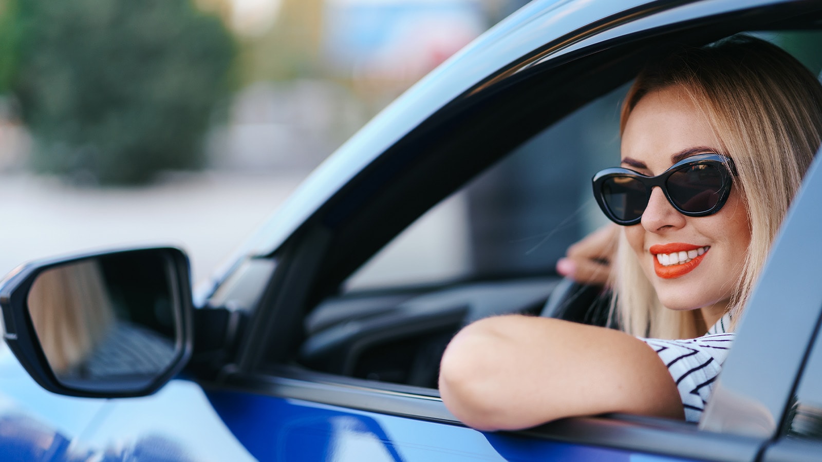 A woman wearing fashionable sunglasses over her contact lenses while driving to provide UV protection and reduce sun glare for safer vision.