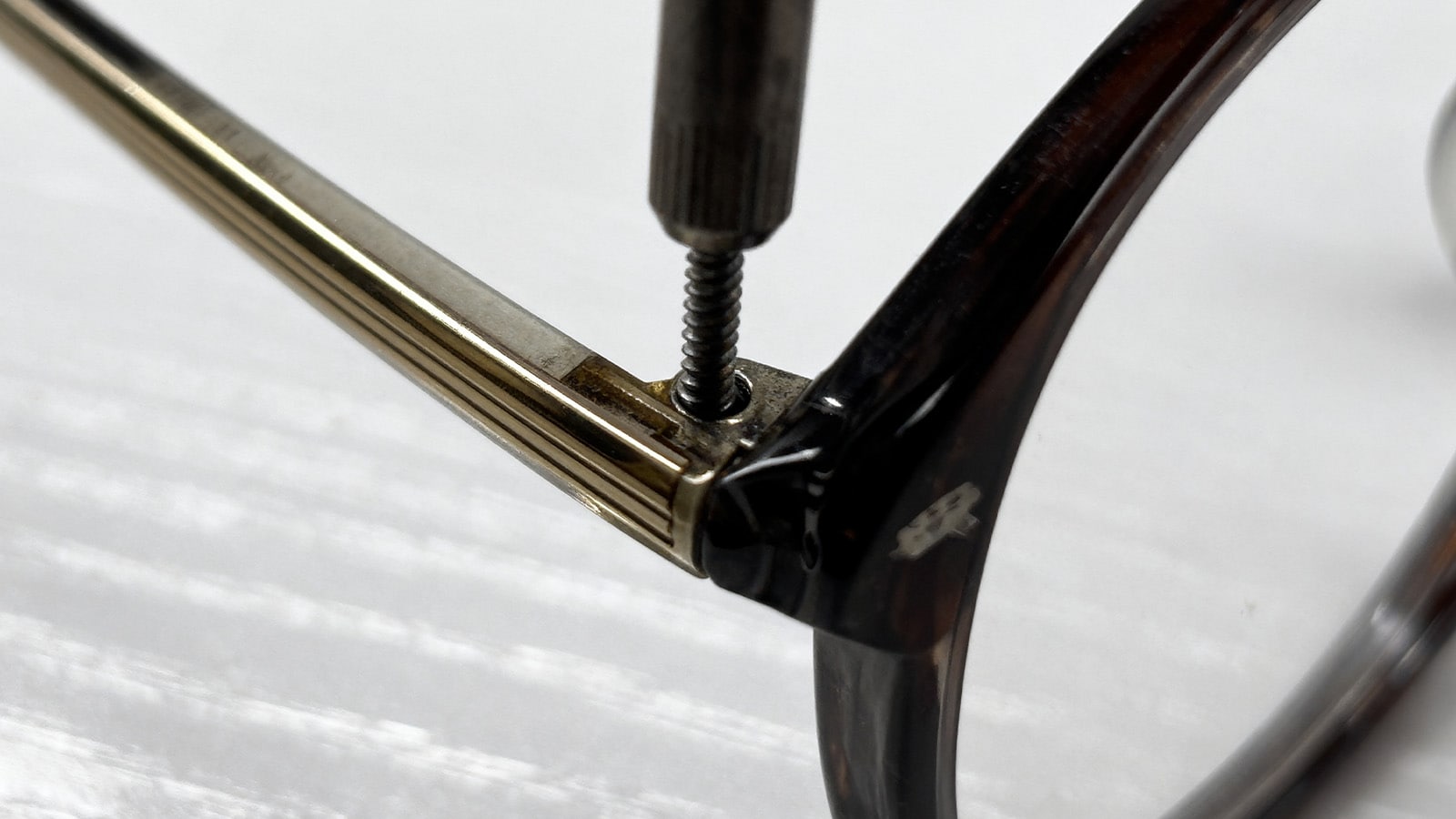 Using a mini-screwdriver from an eyeglass repair kit to tighten a loose hinge screw on a pair of sunglasses frames.