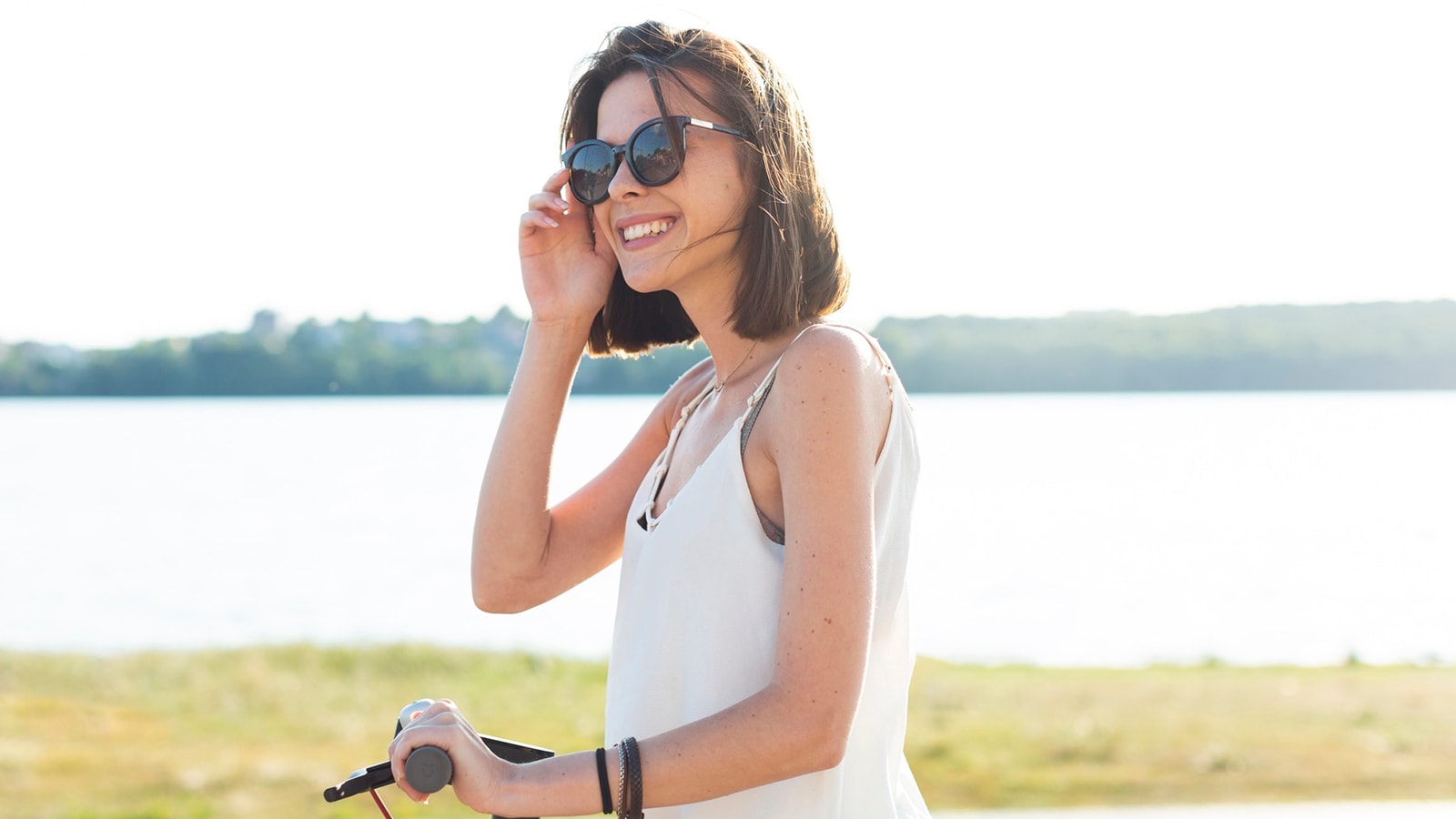 A smiling woman enjoys a sunny day by the water, highlighting the lifestyle benefits of wearing prescription sunglasses for outdoor activities.