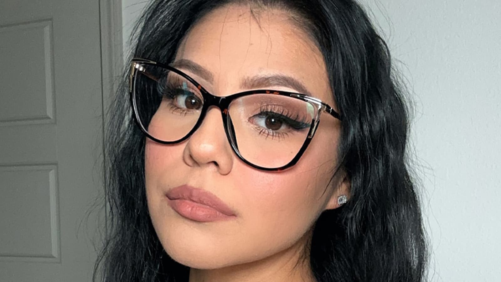 A woman wearing black and gold-rimmed cats-eye glasses and posing for a close-up photo.