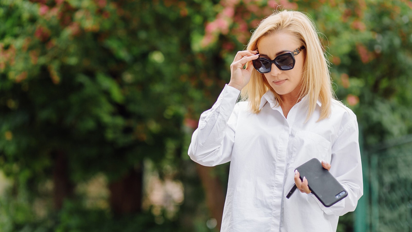 A woman in a white shirt adjusts her stylish prescription sunglasses, showing the convenience of having vision correction and UV protection.