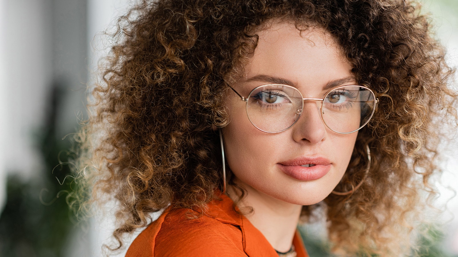Woman with curly hair wearing round gold metal eyeglasses with adjustable nose pads